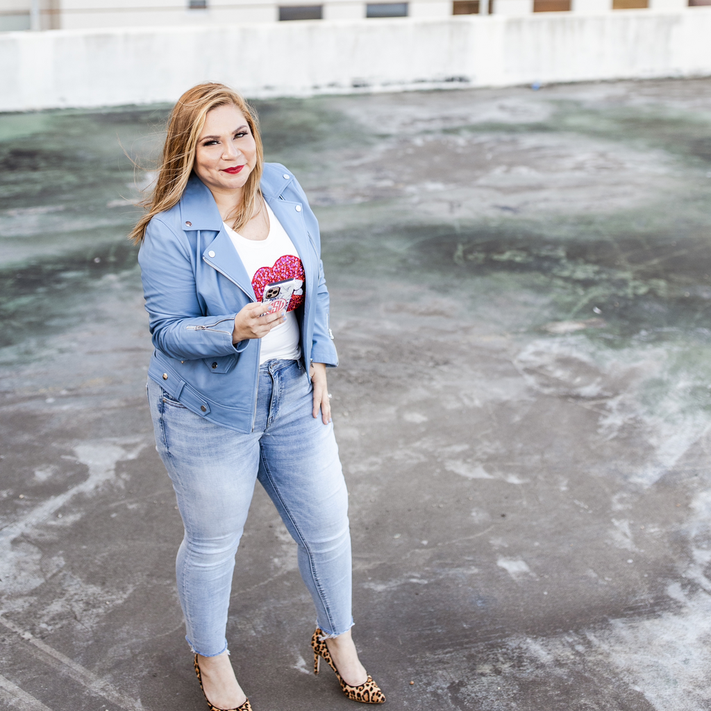 A woman stands on a rooftop wearing denim jeans, a blue jacket, and leopard-print heels, holding a red clutch with hearts. She is smiling at the camera for ESV Creative's social media audit.